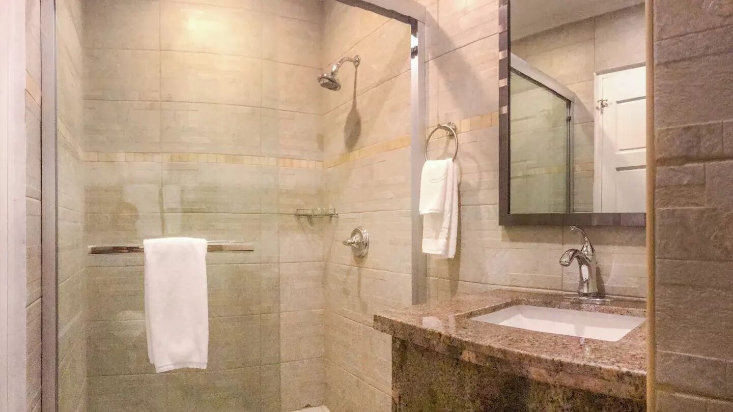 Une salle de bain dotée d’une douche à parois de verre, d’un lavabo avec un plan de toilette en marbre et d’un miroir au-dessus du lavabo.