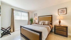 Une chambre à coucher avec un lit, des tables de chevet, une lampe, une plante et une fenêtre avec des rideaux.