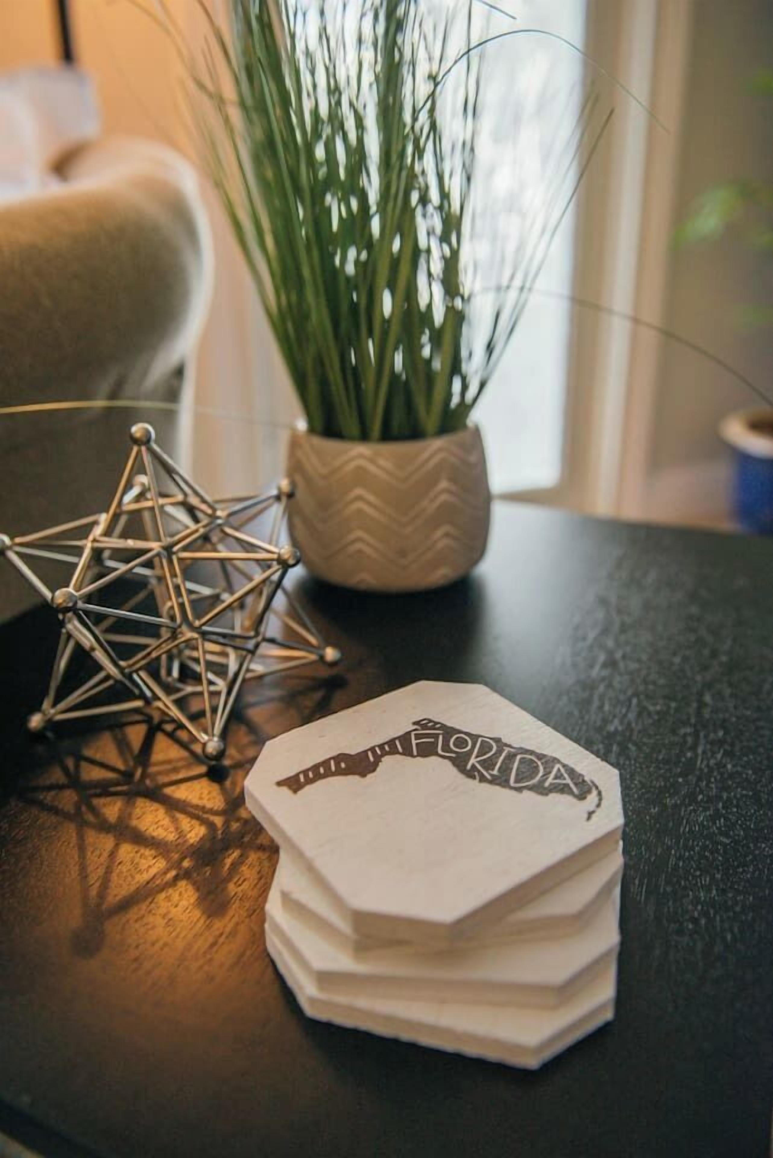 A stack of white cards with "FLORIDA" written on them, placed on a dark surface with a geometric metal sculpture and a potted plant in the background.