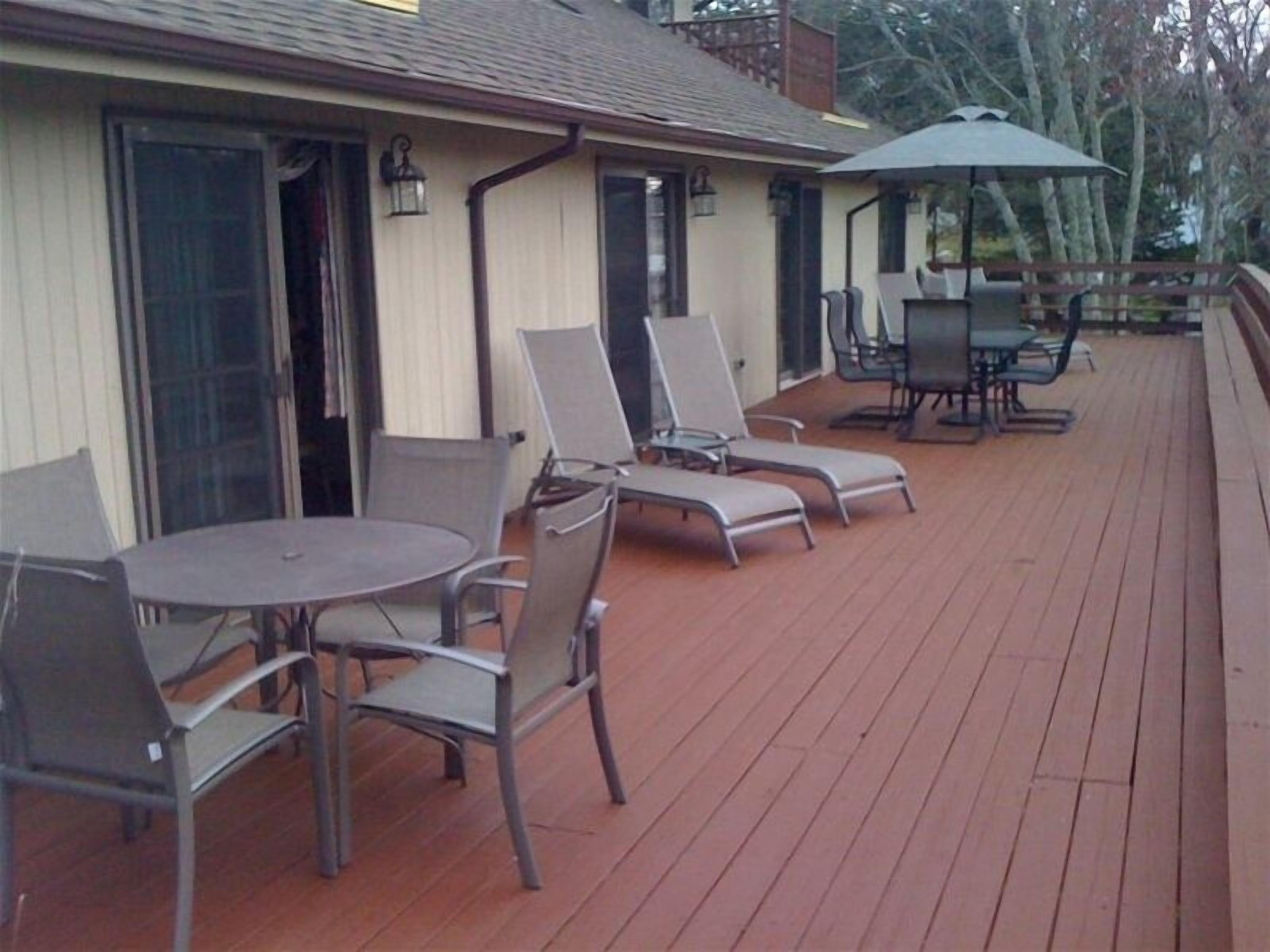 Une terrasse extérieure couverte, dotée de chaises et d’une table en métal, une plateforme avec une rambarde et un espace de détente couvert agrémenté de parasols.