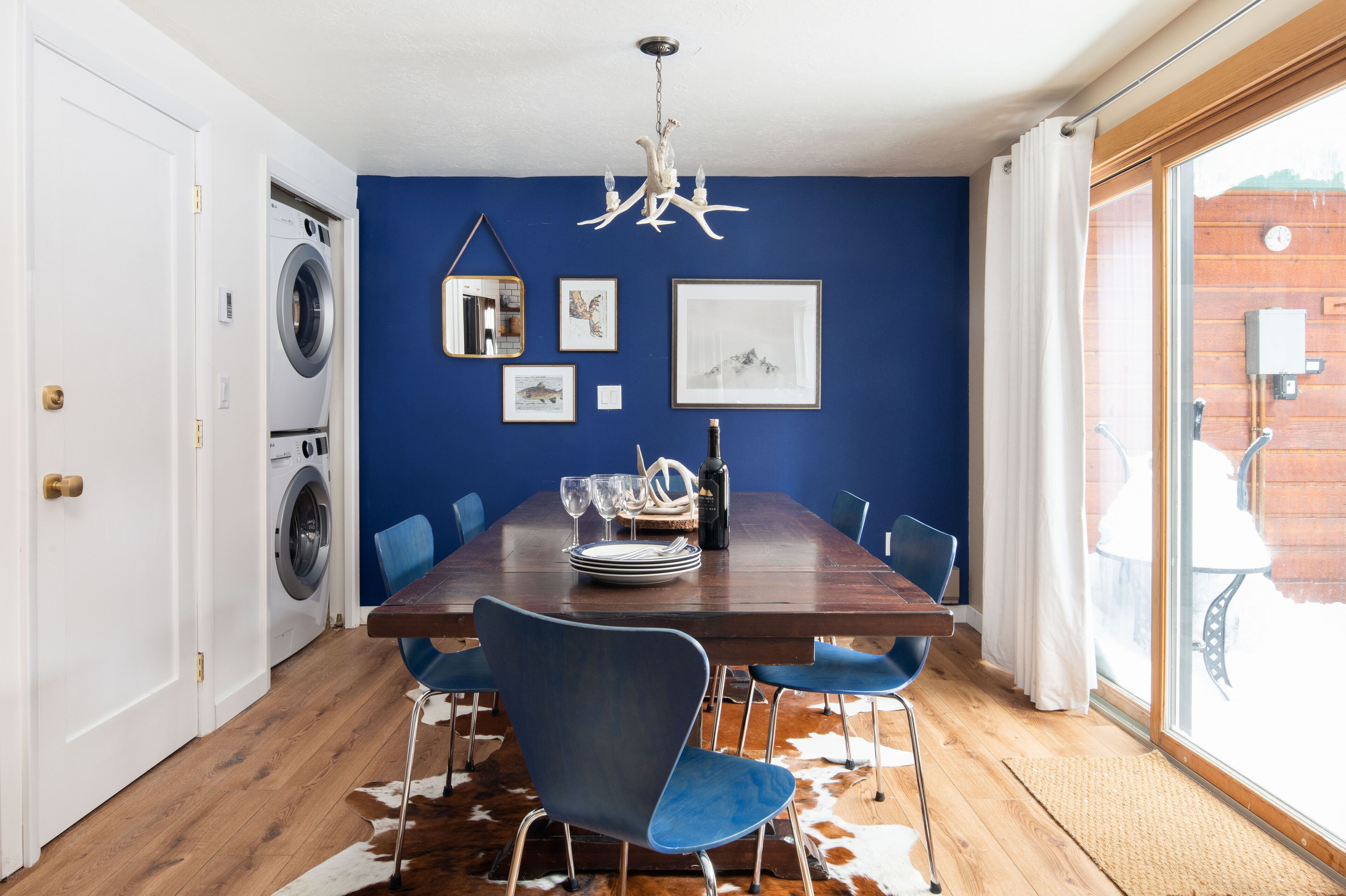 Un comedor con una mesa de madera, sillas azules y un tapiz de cuero de vaca.