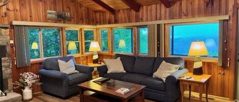 A cozy living room with wooden walls and floors, two sofas, a coffee table, and lamps.