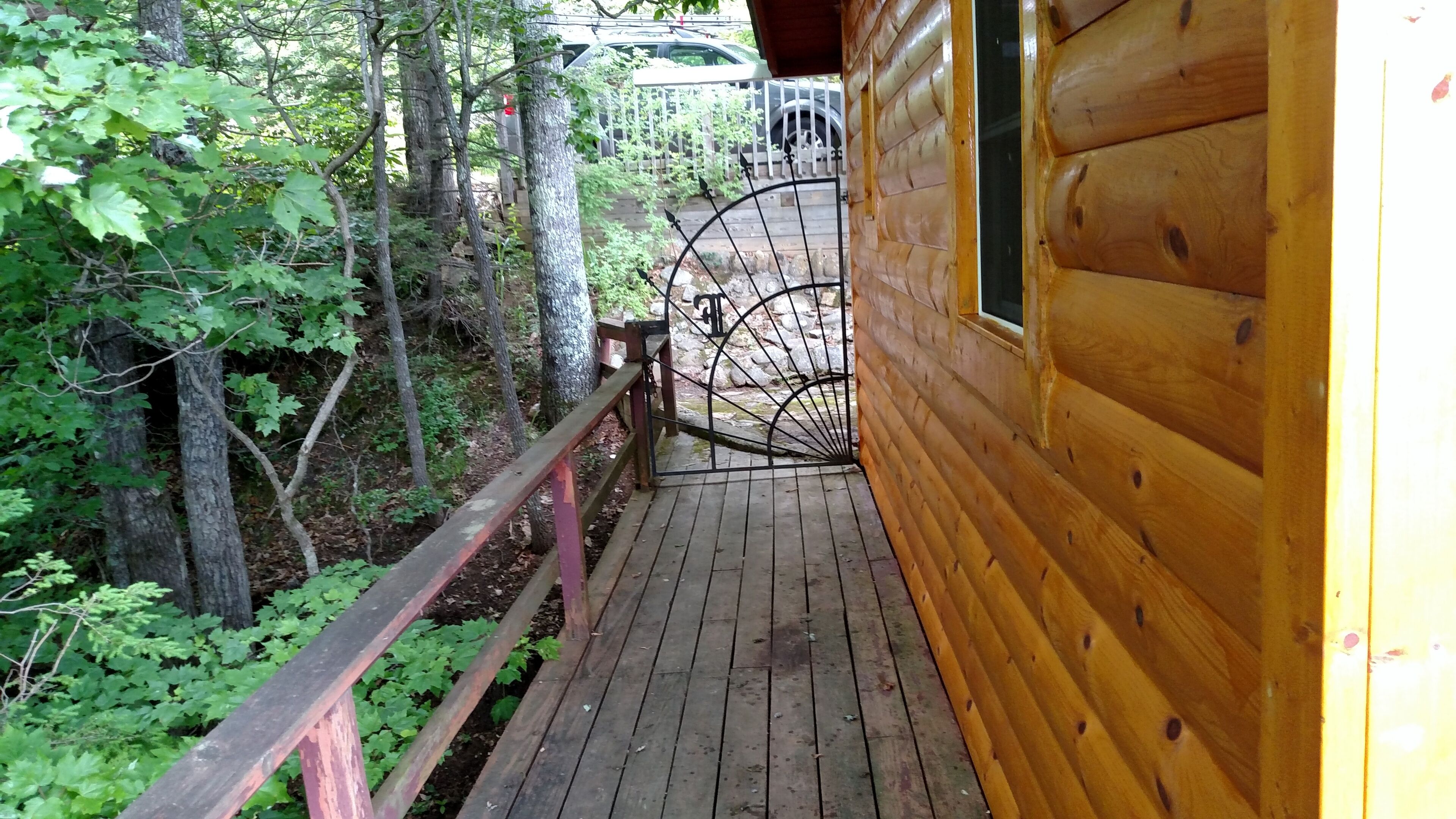 A wooden cabin with a wooden deck leading to a metal gate.