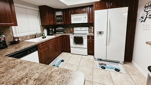 A modern kitchen with dark wooden cabinets, a white refrigerator, a microwave, a stove, and a sink. - Affordable 3 Bedroom Home W / Private Pool. Minutes from Orlando's theme parks (Orlando)