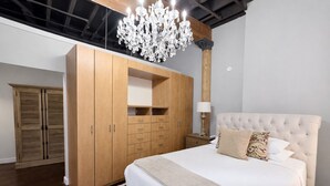 A bedroom with a large bed, wooden wardrobe, and a chandelier. - Downtown Music City Loft living! ~Steps to the Ryman and Broadway. (Nashville)