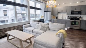 A modern living room with a sofa, a coffee table, and a kitchen area with appliances. - Downtown Music City Loft living! ~Steps to the Ryman and Broadway. (Nashville)