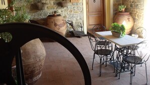 Un muro de piedra rústico con una puerta de madera, una mesa con sillas y plantas en macetas.