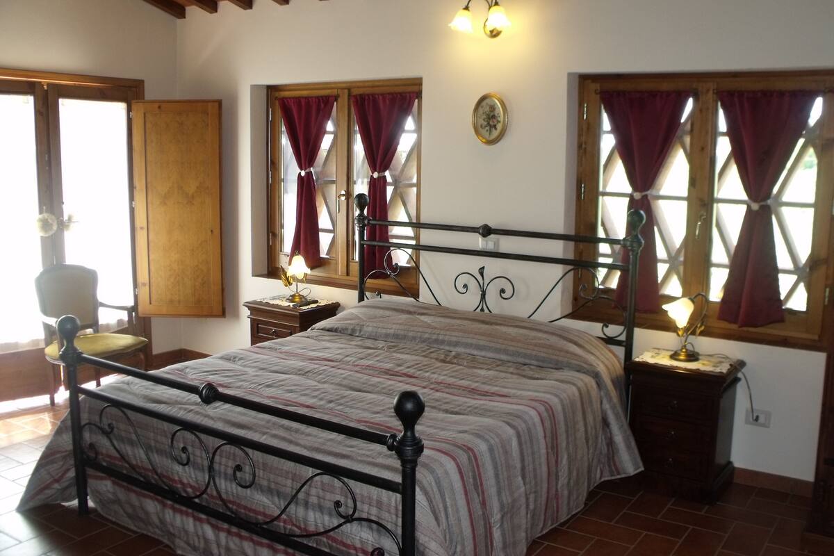A bedroom with a bed, two bedside tables, a chair, and windows with curtains.