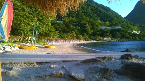 A beach with thatched umbrellas, yellow kayaks, and a mountain backdrop.