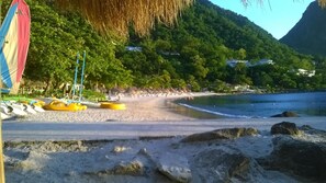 A beach with thatched umbrellas, yellow kayaks, and a mountain backdrop. - Cocoa  Pod Studio (Soufrière)
