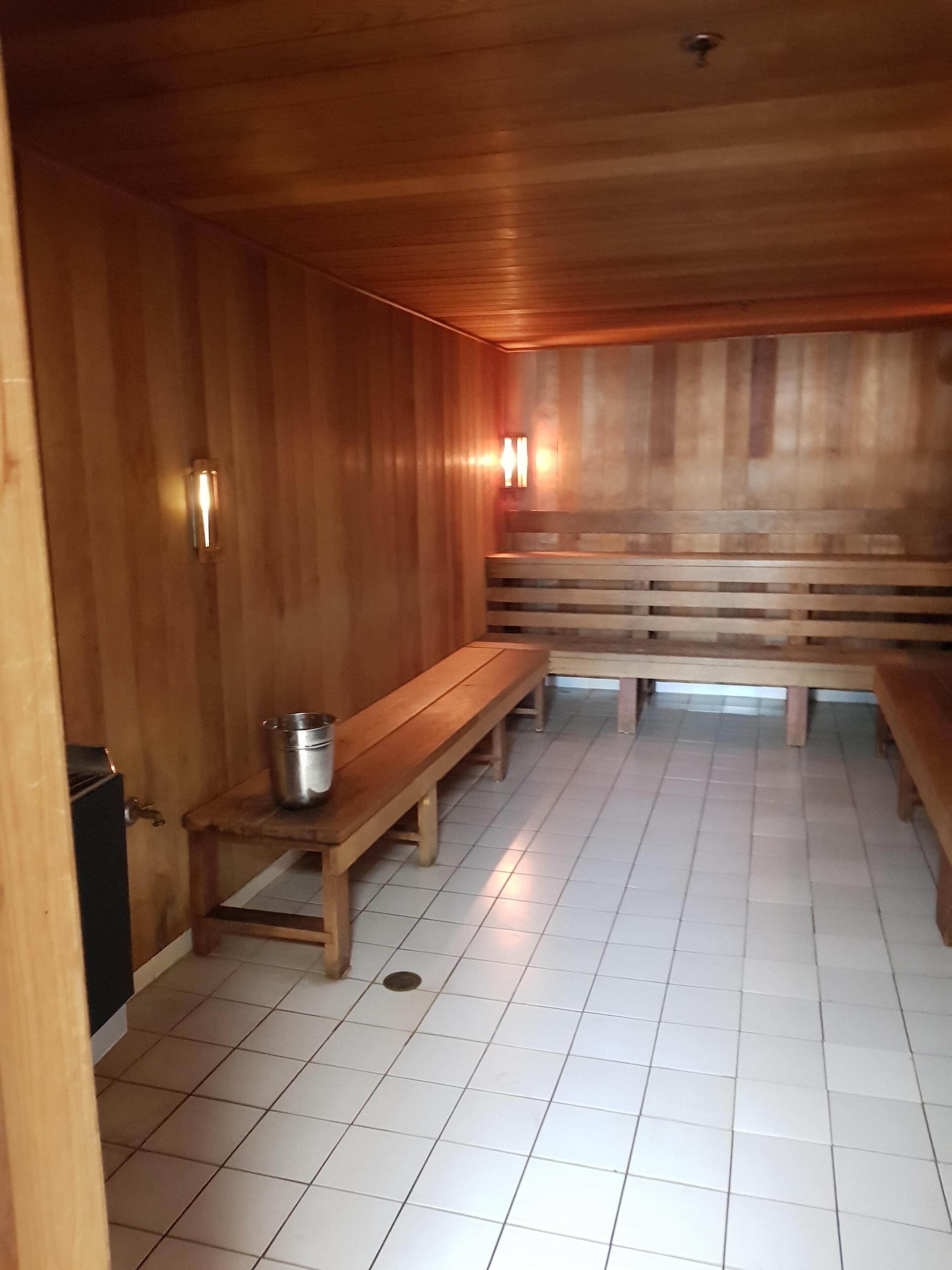A sauna room with wooden benches and a metal bucket.
