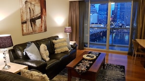 A modern living room with a leather sofa, a coffee table, and a large window offering a city view. - Executive apartment waterfront Darling Harbor ICC Sydney  (Sydney)