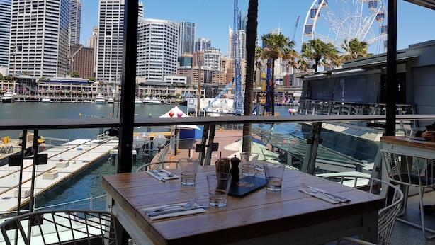 A dining area with a view of a city skyline, including a Ferris wheel, through large windows. - Executive apartment waterfront Darling Harbor ICC Sydney  (Sydney)