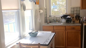 A kitchen with a dining table, chairs, a window with curtains, a clock, and a sink.