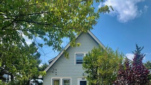 A two-story house with a front porch, a wooden deck, and a small garden with a pathway leading to the house.