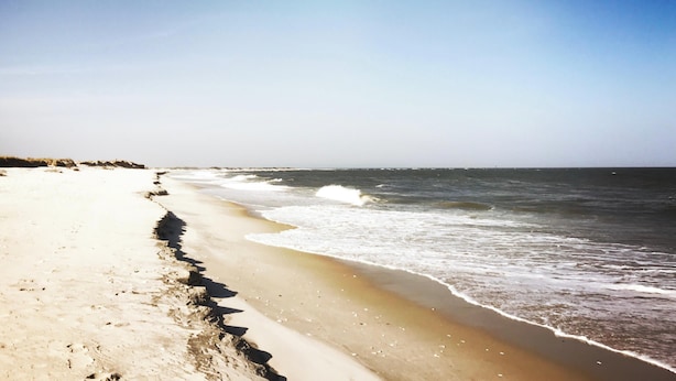 A beach with a long stretch of sandy shore and waves approaching the beach.