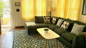 A cozy living room with a green sofa, patterned cushions, a small white table, and a patterned rug.