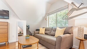 Une chambre mansardée chaleureuse avec un canapé-lit, une table en bois et un téléviseur fixé au mur.