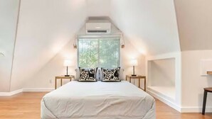 Une chambre à coucher comprenant un lit, deux tables de chevet, une fenêtre et un appareil de climatisation.