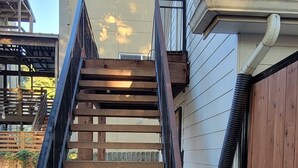 Un escalier en bois mène à une maison dont la façade est de couleur beige et dont la gouttière est noire.