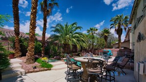 Une terrasse extérieure avec une table ronde et des chaises, entourée de palmiers et d’une piscine.