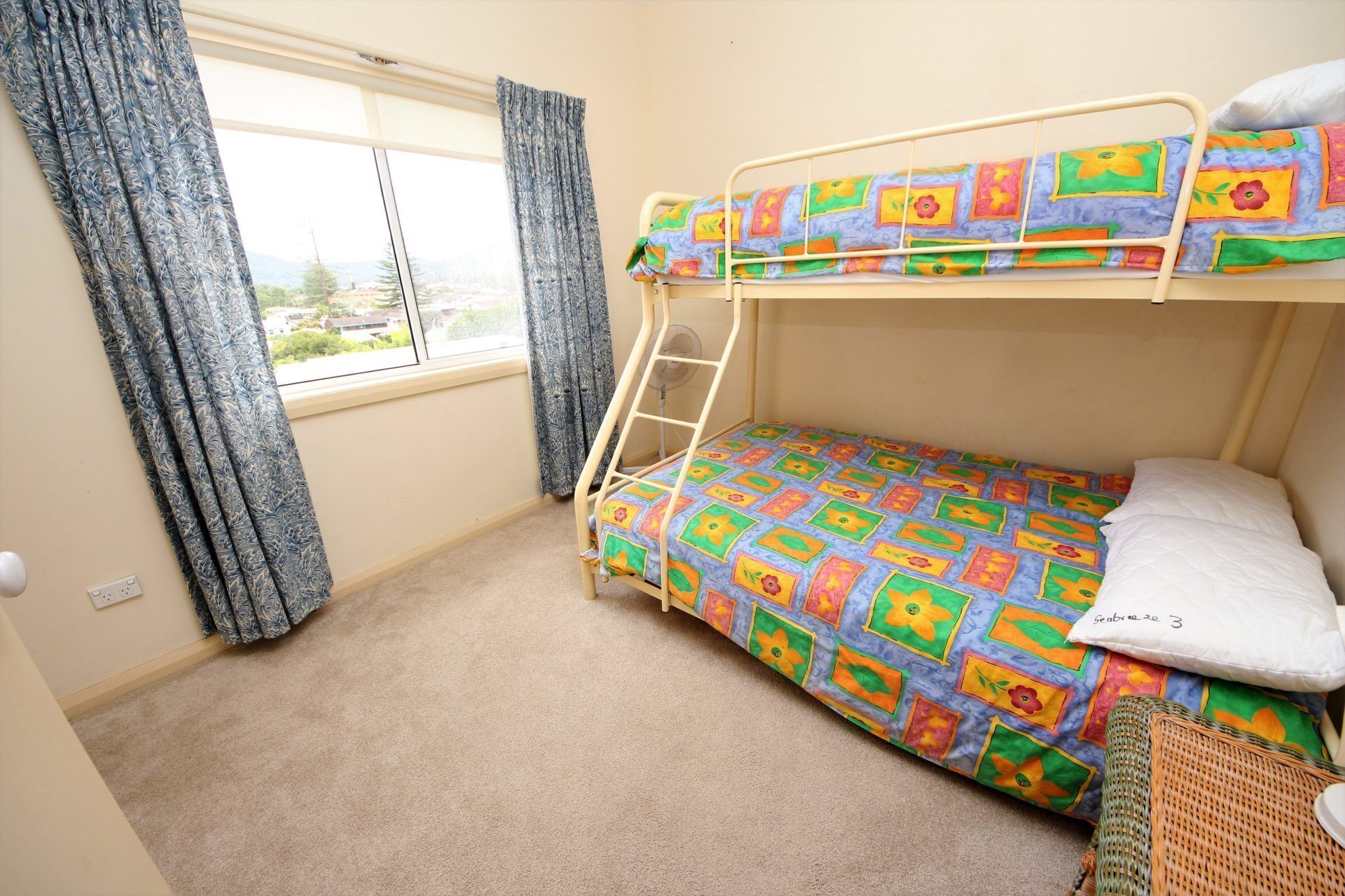 A bunk bed room with a window, curtains, and a fan.