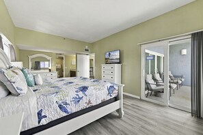 Un dormitorio con cama, cómoda, televisión y puerta corrediza de vidrio que da a un balcón con sillas.