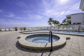 A circular hot tub with a pool in the background, surrounded by a white fence and palm trees.