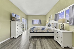 Un dormitorio con cama, cómoda, mesita de noche y una ventana con cortinas.