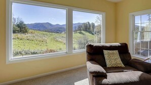 A room with two large windows offering a view of a grassy landscape and mountains.