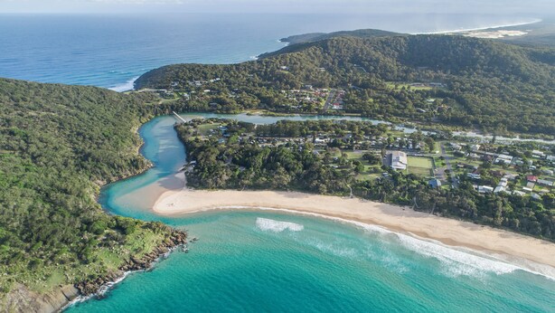Vista aérea de una zona costera con playa, aguas turquesas cristalinas y una combinación de paisajes residenciales y naturales.