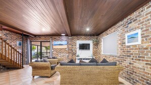 Un espacio de sala acogedor con pared de ladrillo, techo de madera y un televisor grande.