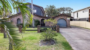 Una casa de dos pisos con fachada de ladrillo, un garaje y un pequeño jardín con una palmera.