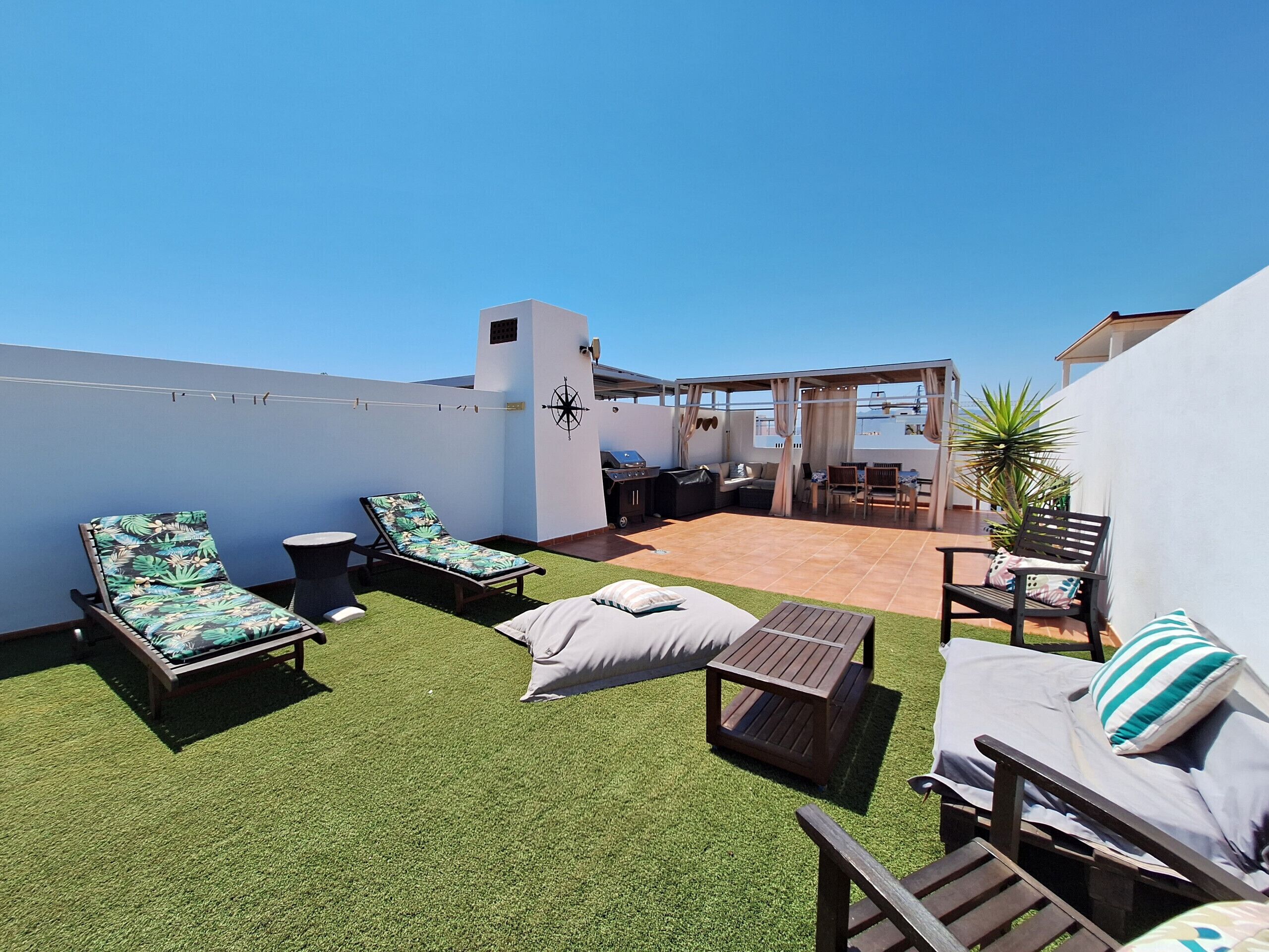 A rooftop terrace with lounge chairs, a small table, and a grill area.