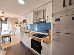 A modern kitchen with white cabinets, a double sink, a stove, and a refrigerator.