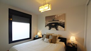 A bedroom with a large bed, two bedside tables with lamps, a window with blinds, and a wall-mounted picture of the Eiffel Tower. - Al 318 - Penthouse with terrace  near the beach (Vera playa)