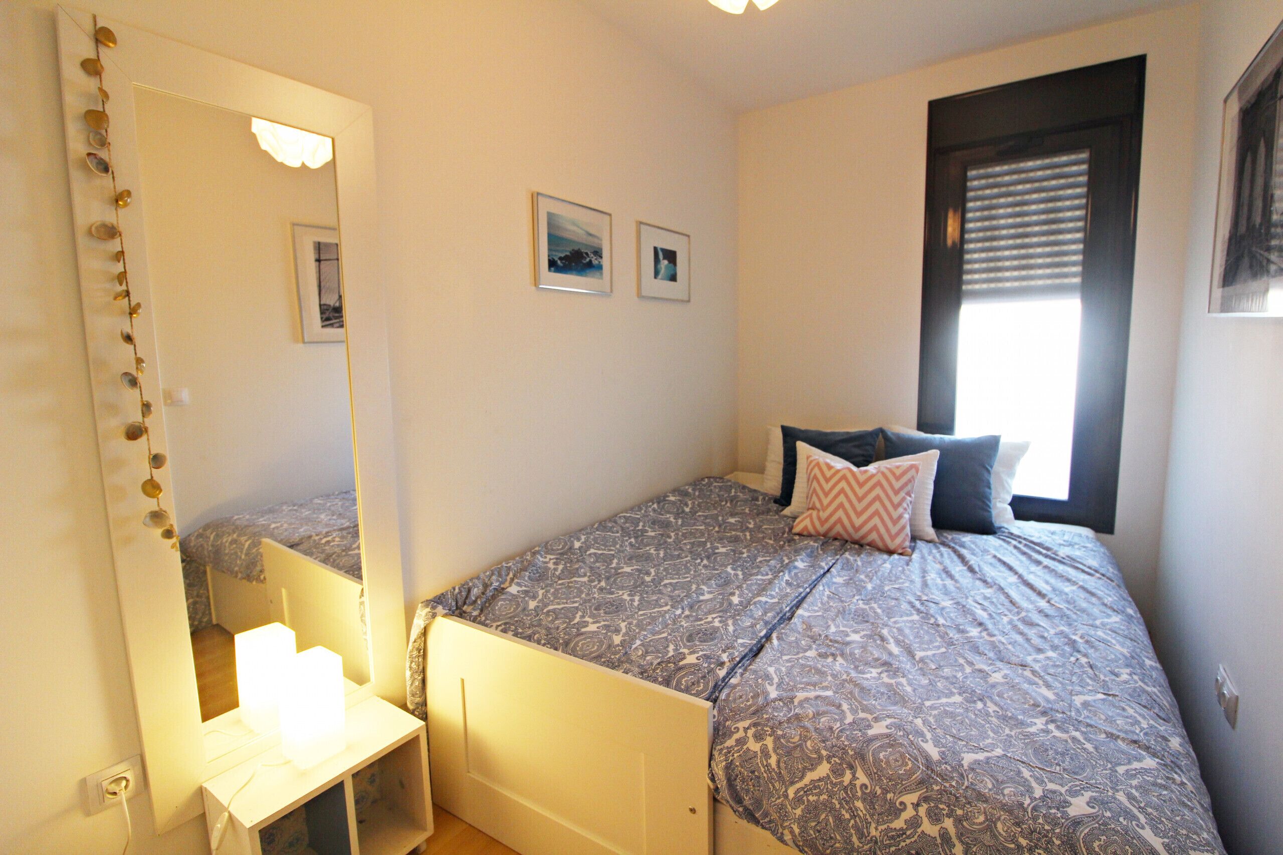 A bedroom with a bed, a bedside table, a mirror, and two framed pictures on the wall.