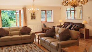 Ein Wohnzimmer mit zwei Sofas, einer Chandelier, einem Spiegel und Blick auf Grünfläche draußen.