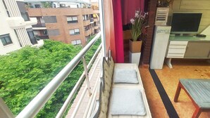 A balcony with a view of buildings and greenery, a small desk with a computer, and a chair. - APARTMENT MAR CENTER ALICANTE IDEAL FOR FAMILIES 👪 GROUPS AND THE DISABLED (Alacant)