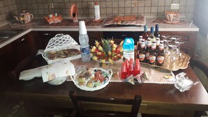 A kitchen with wooden cabinets, a tiled backsplash, and a dining table set with food, drinks, and condiments. - Villa manghisi holiday home (Noto, Siracusa)