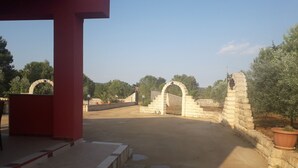 A paved entrance with stone archways, a red structure, and potted plants. - Villa manghisi holiday home (Noto, Siracusa)