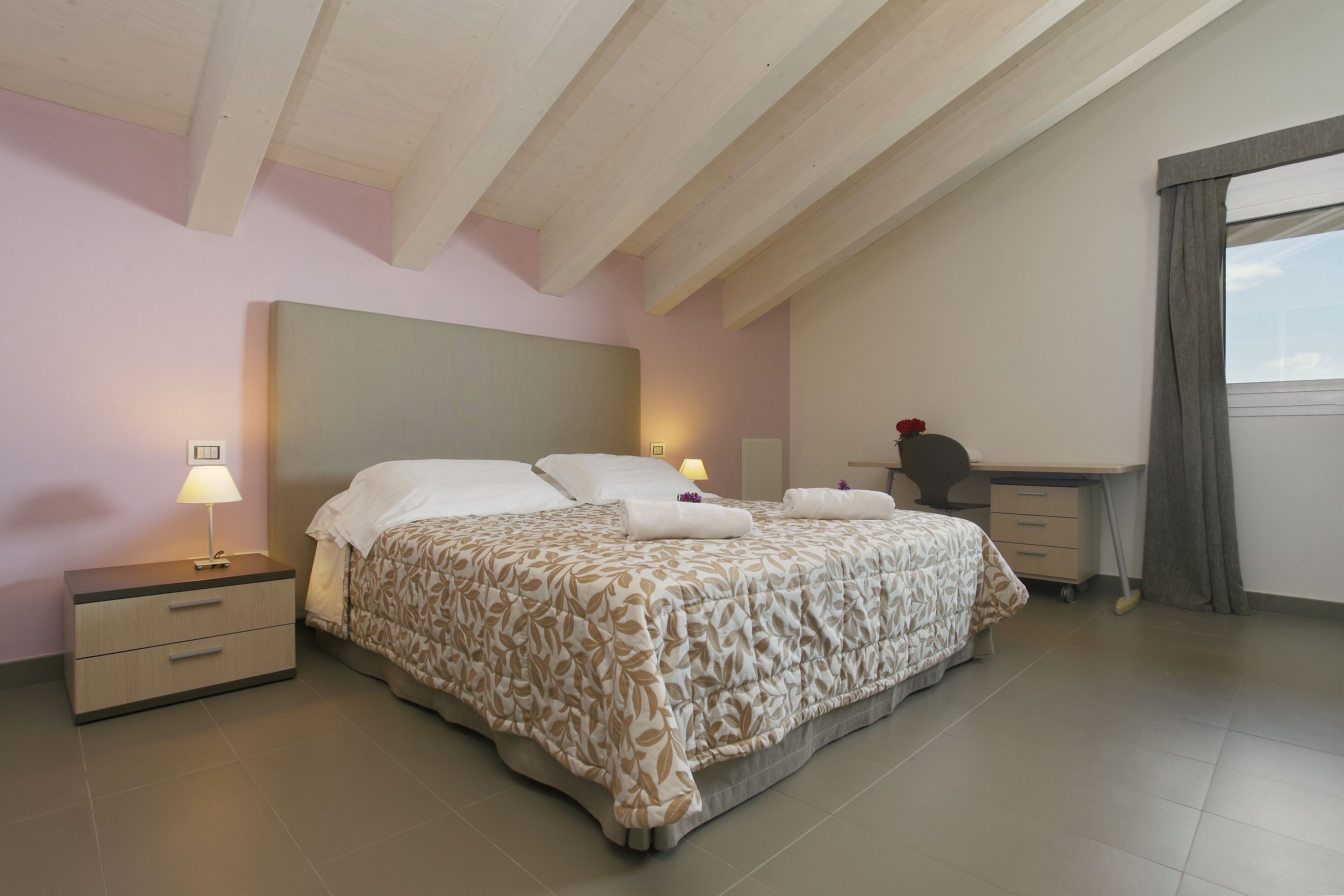 A bedroom with a bed, bedside tables, a desk, and a window.