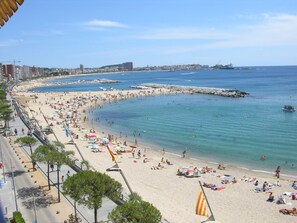 A coastal cityscape with a wide beach, clear skies, and a calm sea.