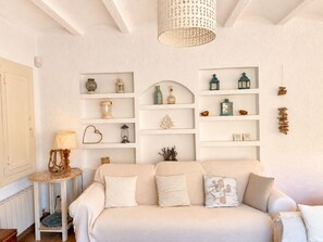 A living room with a beige sofa, a small side table, and shelves with various decorative items. - Formentera on the Costa Brava - BBQ - Garden (Calonge)