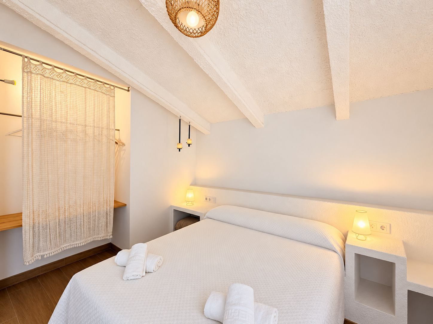 Une chambre d’hôtel avec un lit, des lampes de chevet, un luminaire suspendu et un rideau.