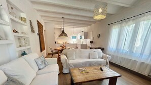 Een ruime woonkamer met een witte bank, een houten salontafel en een keuken op de achtergrond.