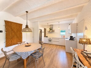 Une cuisine compacte avec des meubles blancs, un îlot central et un coin repas comprenant une table ronde et des chaises.