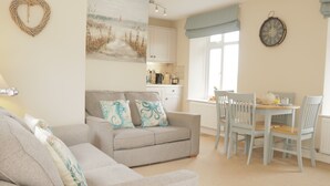 A cozy living room with a grey sofa, a dining table with chairs, and a kitchen in the background. - Apartment set in stunning grounds with coastal views & access to coastal paths (Thurlestone)
