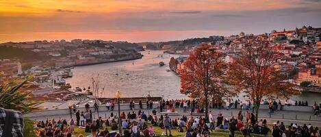A crowded riverside promenade during sunset with people walking and sitting.