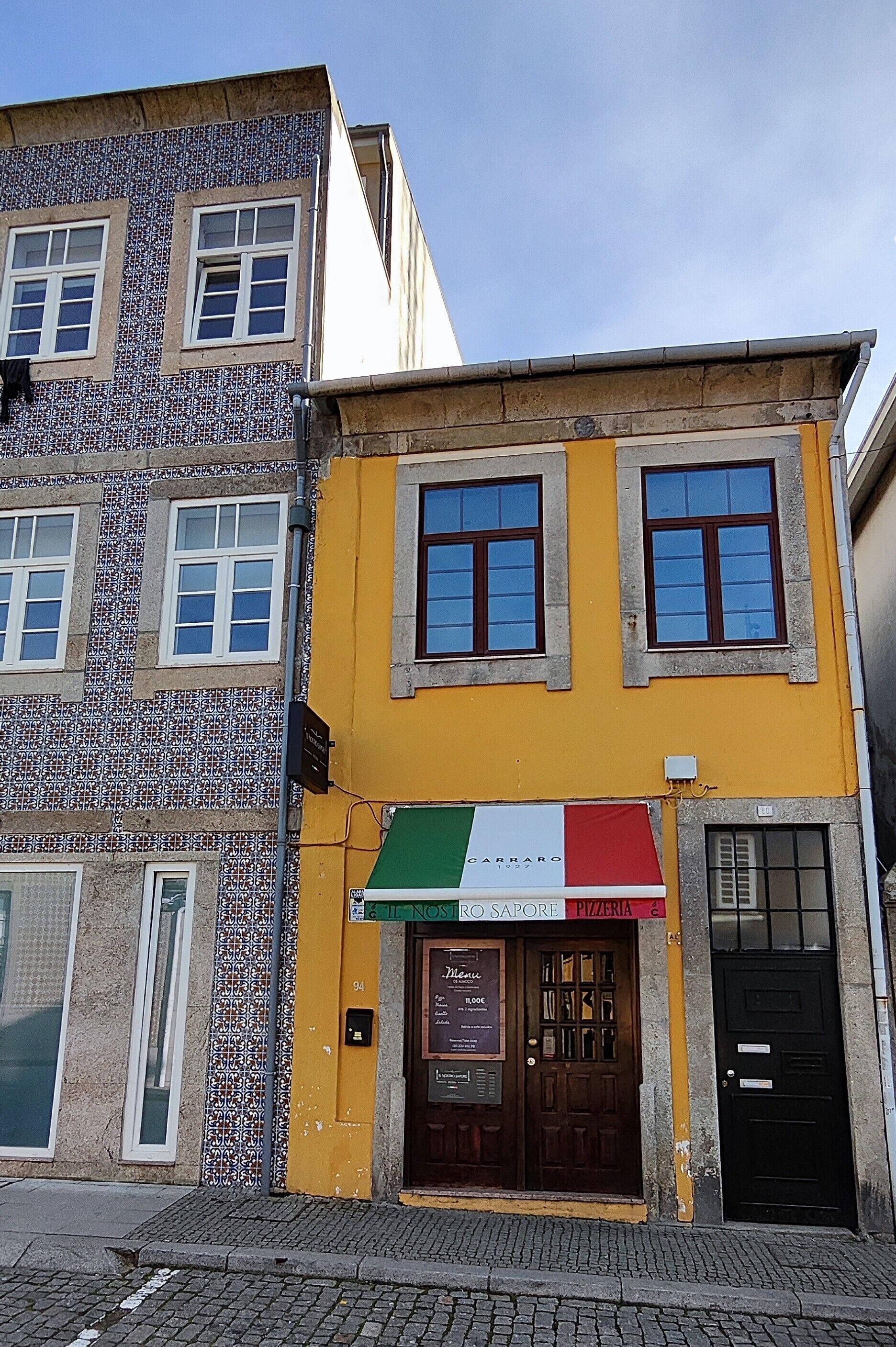 A building with a tiled facade and a storefront with a sign for 'Carraro Pizzeria'.